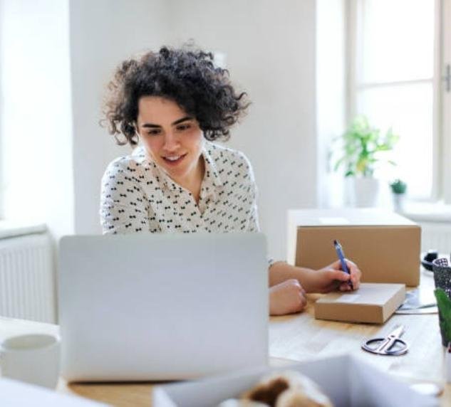 a smiling young woman is writing a blog on her laptop